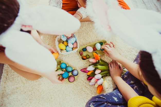 Girlfriends in bunny ears sitting on the floor and playing with Easter rabbit. The concept of preparation for Holiday