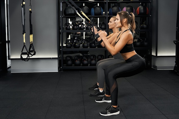 Girlfriends doing squatting with trx system