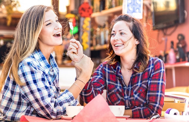 Fidanzate coppia felice bere cappuccino e ridere insieme - concetto di ritrovo con giovani donne che parlano e si divertono al bar - filtro vintage caldo con focus sulla ragazza giusta