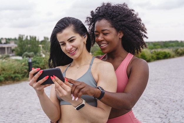 Girlfriends in sportswear using smartphone. Horizontal view of fitness women outdoor with technology