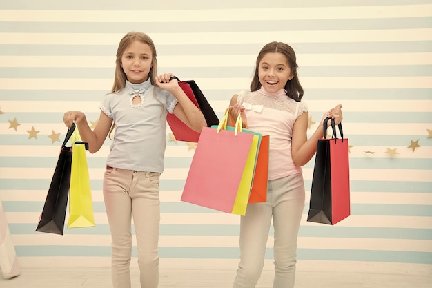 Girlish happiness Kids happy carry bunch packages Shopping with best friend concept Girls like shopping Kids happy small girls hold shopping bags Enjoy shopping with best friend or sister