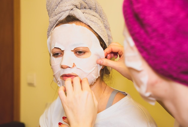 Le ragazze stanno mettendo un foglio di maschera per la pelle sul viso procedure di bellezza a casa