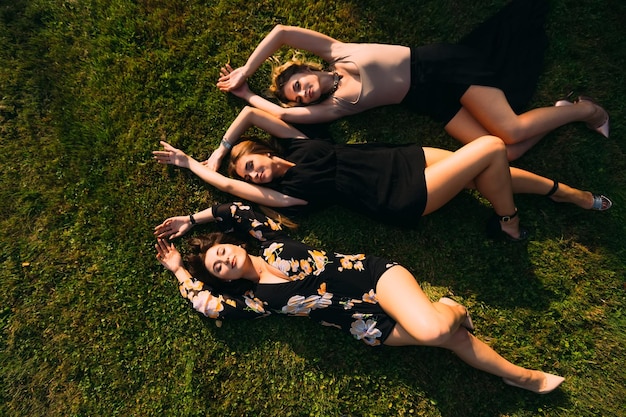 Girls in beautiful dresses lie on the grass and smile top view