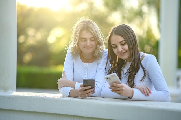 Ragazze bionde e brune in magliette bianche con un telefono all'aperto in estate