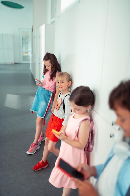 Photo girls and boy standing near lockers and playing on phones