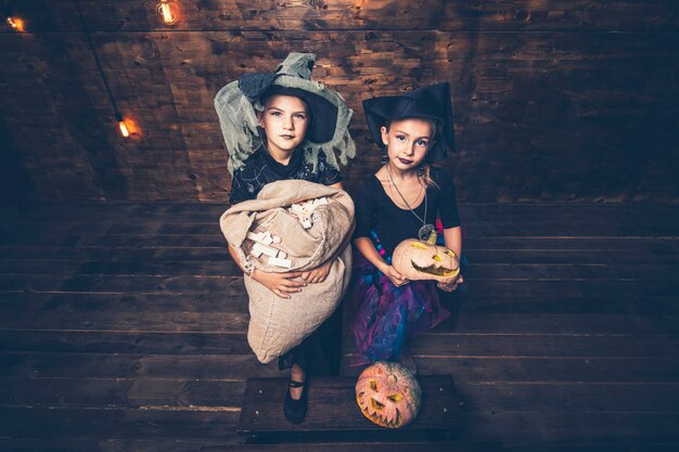 Girls costumes witches with pumpkins and treats in the Halloween on wooden scenery