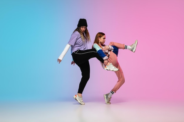 Девушки танцуют хип-хоп в стильной одежде на градиентном фоне в танцевальном зале в неоновом свете