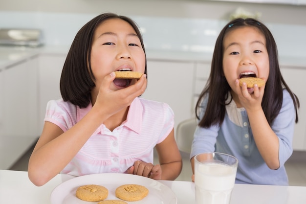 Girls enjoying cookies and milk in kitchen