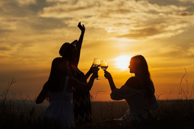 Girls enjoying picnic next to the river. Young friends having fun at hill after sunset.