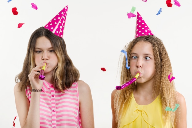 Ragazze in cappelli festosi, che soffia nei tubi, coriandoli colorati