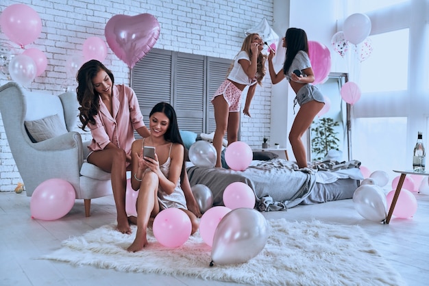 Girls fun. Four attractive young women in pajamas smiling while having a slumber party in the bedroom with balloons all over the place