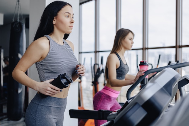 Le ragazze in palestra sono addestrate su tapis roulant e bevono acqua, sorridendo