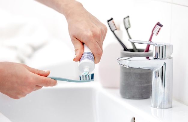 Photo girls hand applies toothpaste on brush for hygiene in pristine white bathroom