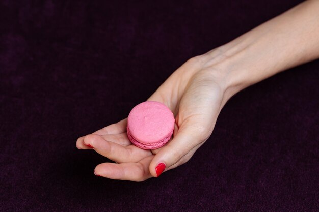 Foto la mano delle ragazze con la manicure rosa brillante tiene le metà rosa brillante dei macaroni