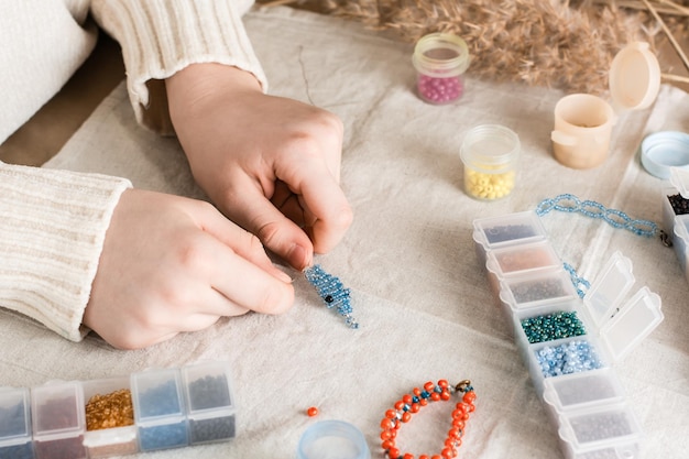 Photo the girls hands are weaving a dolphin on a table with items for beading