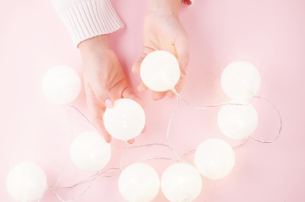 Girls hands holding light garland on pink pastel background