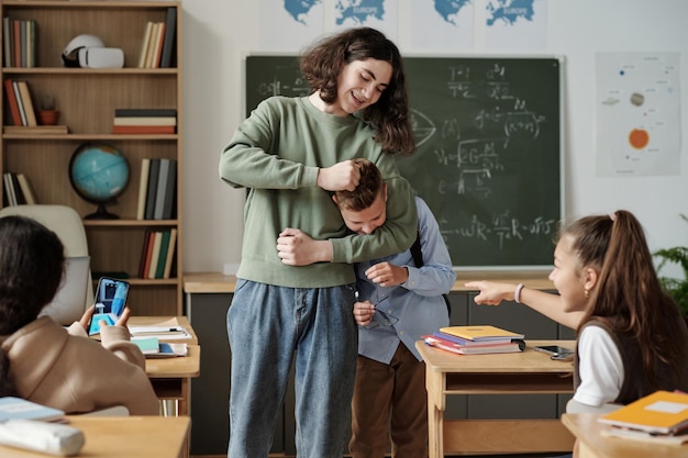 Girls laughing at junior school learner while their classmate fighting with him