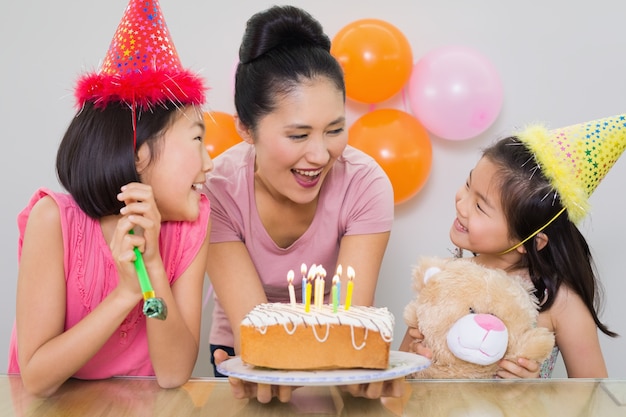 Girls looking at mother with cake at a birthday party