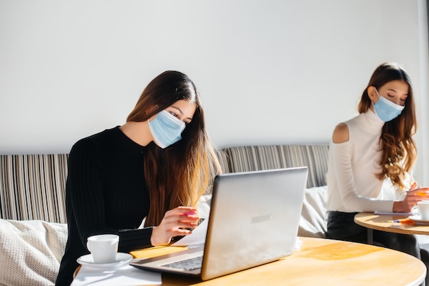 Girls in masks sit in the office and work on a laptop.