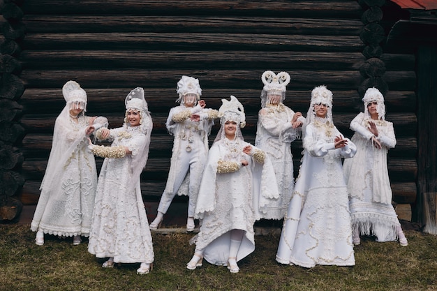 Girls new ethnic Russian fashion Vogue creative clothes pose near old house, white dress and hat, ethnic clothing, Russian fashion. Fancy dresses, young girls together. ,   