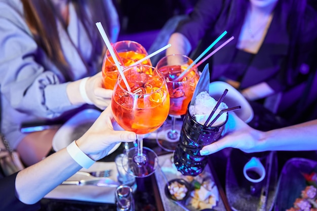 Photo girls in a nightclub clink glasses with alcoholic drinks