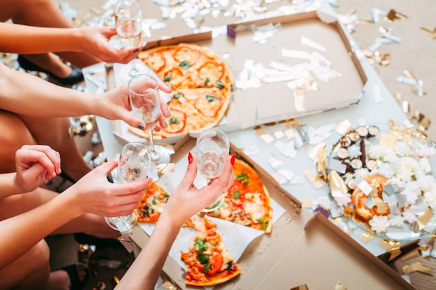 Foto festa delle ragazze. ritagliata colpo di donne in giro, sedute davanti alla pizza in scatole, con in mano bicchieri di champagne.