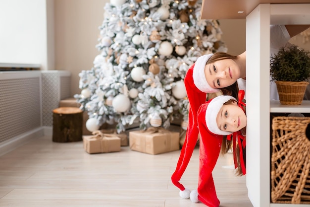 Girls in a red santa hats looks out from behind the kitchen table with a beautiful snowcovered