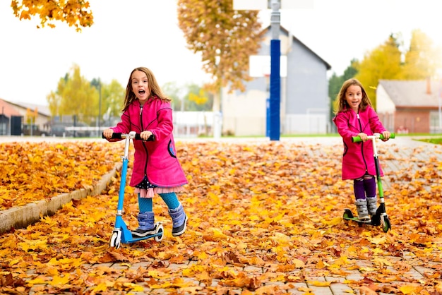 Girls riding push scooters at park during autumn