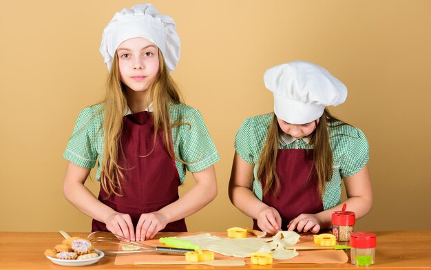 生姜生地を楽しんでいる女の子姉妹自家製クッキー最高の子供たち一緒にクッキーを焼く子供たちのエプロンとシェフの帽子料理家族のレシピ料理教育母の日生姜クッキーを焼く