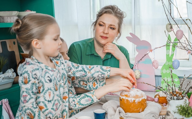 Girls sisters mother at table with Easter decoration Celebration in kitchenTablescape for home Easter holidayFamily religious traditional festive food meal Colored eggscake fun bunny ears