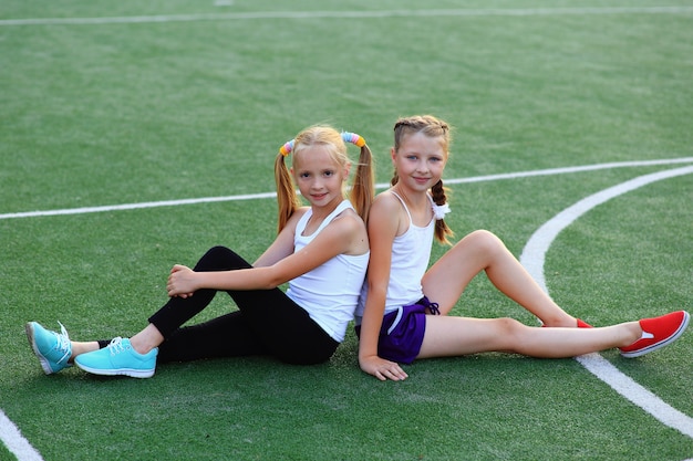 Photo girls sit on a twine on a sports field.