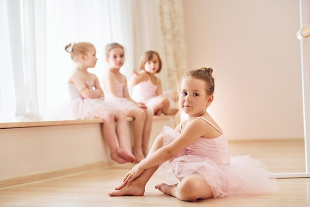 Photo girls sits on windowsill and on the floor little ballerinas preparing for performance