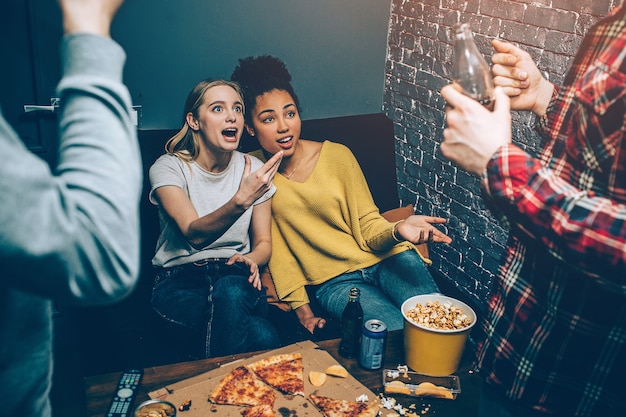 Foto ragazze che si siedono sul divano nero e che parlano con ragazzi molto rumorosi