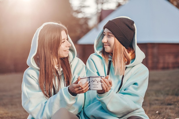 Photo girls spend time in the open nature. they are sitting next to each other holding white mugs with hot drinks in their hands. pleasant and cheerful atmosphere.