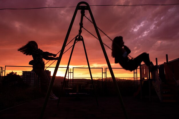 Foto ragazze su una silhouette d'altalena al tramonto