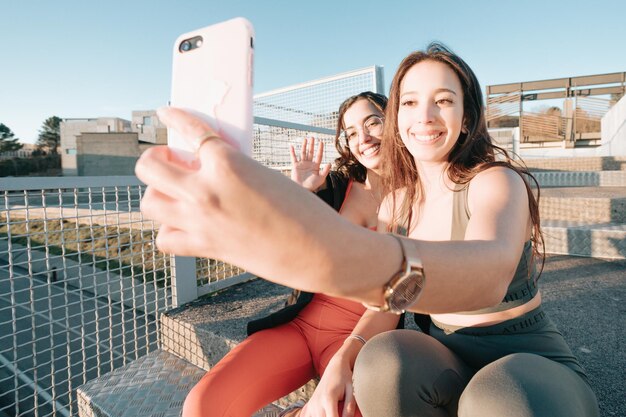 Girls taking a selfie while resting from work out sitting on stairs, modern sporty youngsters recording a video for social networks while smiling. Good vibes and happiness concept. African girls