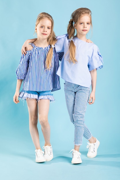 Girls twins in light blue clothes are posing  a blue  .