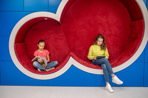 Girls with book and tablet sitting in lounge zone