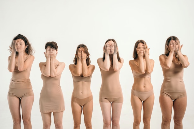 Photo girls with different figures in beige underwear the girls cover their faces with their hands a place...