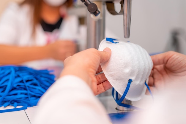 Girls work at the machine for the manufacture of medical masks with nanofibre and solder the loops to them with ultrasound Coronovirus and Covid19 Prevention