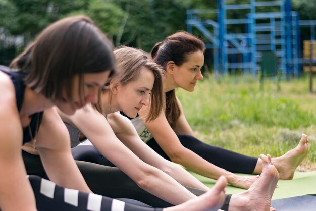 Foto ragazze su materassini da yoga che fanno esercizi di allungamento muscolare della coscia gruppo di giovani donne su lezioni di fitness in natura yoga mattutino