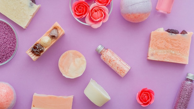 Girly schoonheidsproducten, badhygiëne spa-producten. Roze beautyproducten bath bombs, bath beads, aromatische oliën en rozenzeep. Plat lag op paarse achtergrond. hygiënische toiletartikelen