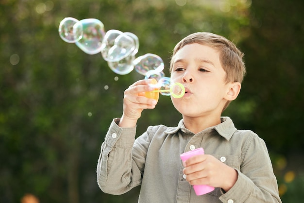 Дайте ребенку мыльные пузыри, и они будут развлечены. Снимок очаровательного маленького мальчика, пускающего пузыри снаружи.