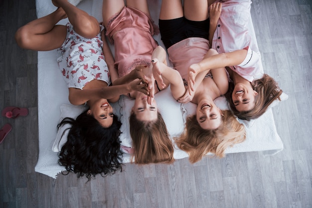 Give high five everyone. Inverted portrait of charming girls that lying on bed in nightwear. Top view