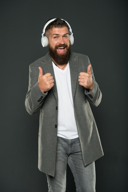 Give thumbs ups to technology. Happy hipster wear wireless headphones. Bearded man enjoy listening to music. Stereo sound technology. New technology. Technology for business and fun.