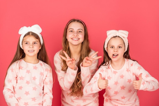 Giving double thumbs and vsigns gestures Happy girls in homewear pink background Children homewear