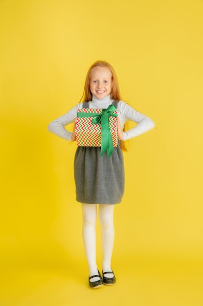 Giving and getting presents on Christmas holidays. Teen girl having fun isolated on yellow studio