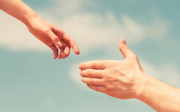 Giving a helping hand. hands of man and woman on blue sky\
background. lending a helping hand. solidarity, compassion, and\
charity, rescue. hands of man and woman reaching to each other,\
support