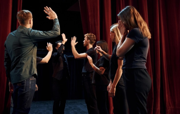 Giving high five celebrating success Group of actors in dark colored clothes on rehearsal in the theater