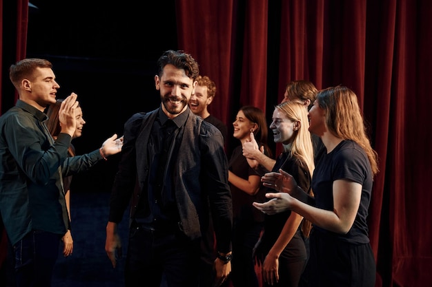 Foto dare il cinque per celebrare il successo gruppo di attori in abiti scuri durante le prove a teatro